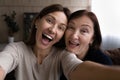 Joyful grown daughter taking funny selfie together with retired mother