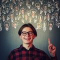 Joyful guy pointing index finger up, showing multiple light bulbs as creative ideas isolated on grey wall background. Positive Royalty Free Stock Photo