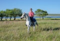 Joyful guy rides on horseback across the field, against the backdrop of the lake.