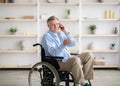 Joyful handicapped senior man in wheelchair taking on smartphone at retirement home Royalty Free Stock Photo