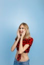 Joyful handsome young blond girl with blue eyes wearing red checkered shirt and blue jeans, with hands on her head