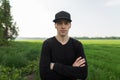 Joyful handsome young man in a fashionable black cap in a stylish t-shirt is resting standing in a field among green grass. Happy Royalty Free Stock Photo