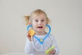 Joyful happy baby girl imagines as doctor at hospital using toy stethoscope and syringe. Royalty Free Stock Photo