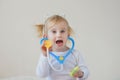 Joyful happy baby girl imagines as doctor at hospital using toy stethoscope and syringe. Royalty Free Stock Photo