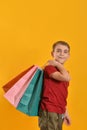 A joyful and happy buyer with colored bags in his hand shows his positive emotions from purchases. Baby with purchases on a yellow Royalty Free Stock Photo