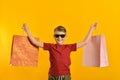 A joyful and happy buyer with colored bags in his hand shows his positive emotions from purchases. Baby with purchases on a yellow Royalty Free Stock Photo