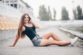 Joyful happy girl sits on the road against background of rostrum. Girl in cheerful mood outdoors Royalty Free Stock Photo