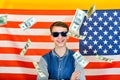 Joyful and happy guy in sunglasses on the background of the American flag, dollars are falling from above, the concept of Royalty Free Stock Photo