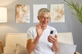 Joyful happy older cellphone user man wearing white T-shirt waving hand hello at gadget frontal camera, speaking on video call,