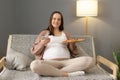 Joyful happy pregnant woman eating pizza alone at home scrolling online using cell phone browsing internet chatting with friends Royalty Free Stock Photo