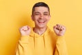 Joyful happy smiling man wearing casual hoodie clenched fists celebrating success rejoicing his achievements posing isolated over Royalty Free Stock Photo