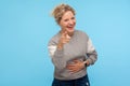 Joyful happy woman with short curly hair in sweatshirt pointing at camera, holding her stomach and laughing at crazy joke