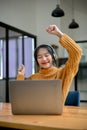 Joyful and happy young Asian female sits at her desk, dancing, enjoys listening to music Royalty Free Stock Photo