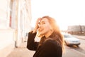 Joyful happy young woman in a black vintage coat with golden earrings enjoys an orange bright sunset standing in the city Royalty Free Stock Photo