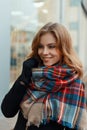 Joyful happy young woman in a fashionable warm wool scarf in a stylish black coat in black gloves is standing and smiling