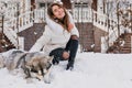 Joyful happy young woman having fun with cute husky dog in snow on street. Cheerful mood, winter snowing time, waiting