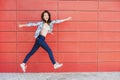 Joyful happy young woman jumping against red wall. Excited beautiful girl portrait