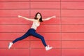 Joyful happy young woman jumping against red wall. Excited beautiful girl portrait