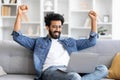 Joyful indian man raising fists in victory while looking at laptop screen