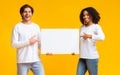 Joyful interracial couple pointing at white blank placard in their hands Royalty Free Stock Photo