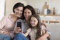 Joyful kid girl, mom, grandma relaxing on sofa with smartphone Royalty Free Stock Photo