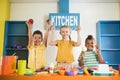 Joyful kids holding plastic tableware at toy kitchen. Royalty Free Stock Photo