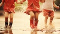 Joyful kids in red rain boots splashing in summer puddles as rain showers embrace them