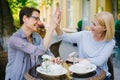 Joyful ladies chatting doing high-five in outdoor cafe in city street