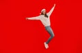 Joyful lady jumping with arms spread wide on red background