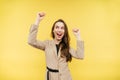 Joyful lady in a suit emotionally rejoices in victory and a yellow background with raised hands. Portrait of a happy woman