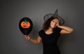 Joyful laughing woman in magic Halloween wizard hat looks at camera, holds black balloon with felt-cut pumpkin, smiles with