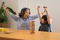 Joyful little asian child and middle aged grandma enjoy playing wood block stacking board game, spending leisure weekend