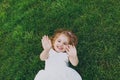 Joyful little cute child baby girl in light dress lie on green grass lawn, showing palms on camera in park. Mother Royalty Free Stock Photo