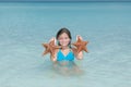 Joyful little girl caught two starfish in tranquil azure ocean Royalty Free Stock Photo