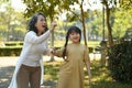 Joyful little girl and grandmother walking in public park surrounded by green trees at sunlight morning. Family