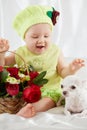 Joyful little girl in greenish clothes and hat sits on bedding