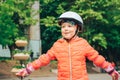 A joyful little girl in a helmet puts her hands to the sides. Beautiful child plays outdoors in the city park