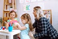 Joyful little girls fold colored cubes on desk in playroom of kindergarten. Young educator sitting with children at