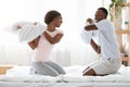 Joyful loving black couple fighting with pillows in bed