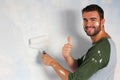 Joyful male painting a wall with a roller and giving a hands up