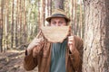 A joyful man in a hat holds a segment from a cut tree imitating a smile