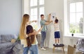 Joyful man and his little son together hang picture on wall under guidance of woman and daughter. Royalty Free Stock Photo