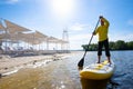 Joyful man sails on a SUP board in large river along the beach