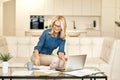 Joyful mature business woman in casual wear making notes, working from home while sitting on a couch in front of laptop Royalty Free Stock Photo