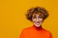 Joyful middle-aged ginger woman looking at camera isolated over yellow background