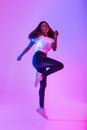 Joyful millennial African American woman flying in air, jumping, smiling at camera in neon light, full length portrait