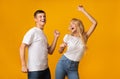 Joyful millennial guy and girl dancing over yellow studio background