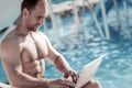 Joyful millennial guy working on laptop at pool