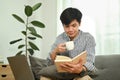 Joyful millennial man drinking coffee and checking his working schedule plan in cozy living room