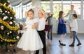 Little children practicing waltz dance in school-hall decorated with Christmas-tree